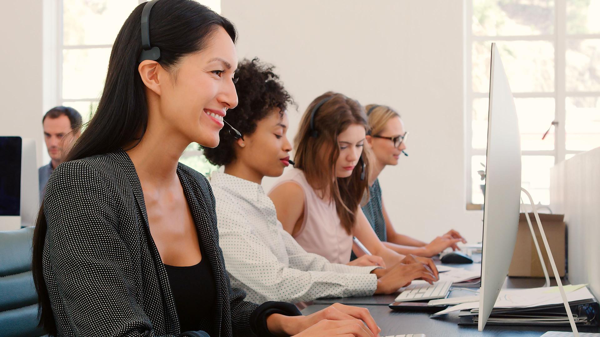 Multi-Cultural Female Business Team Wearing Headsets Working In Busy Customer Service Department