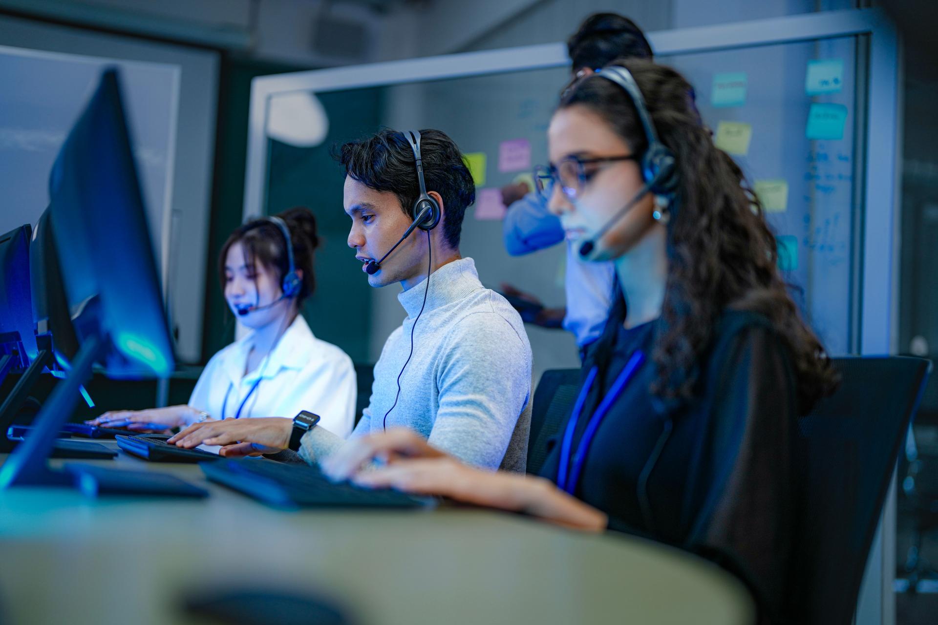 A diverse team of customer service agents wearing headsets works in a modern call center. Professional operators provide technical support and assistance to clients day and night.