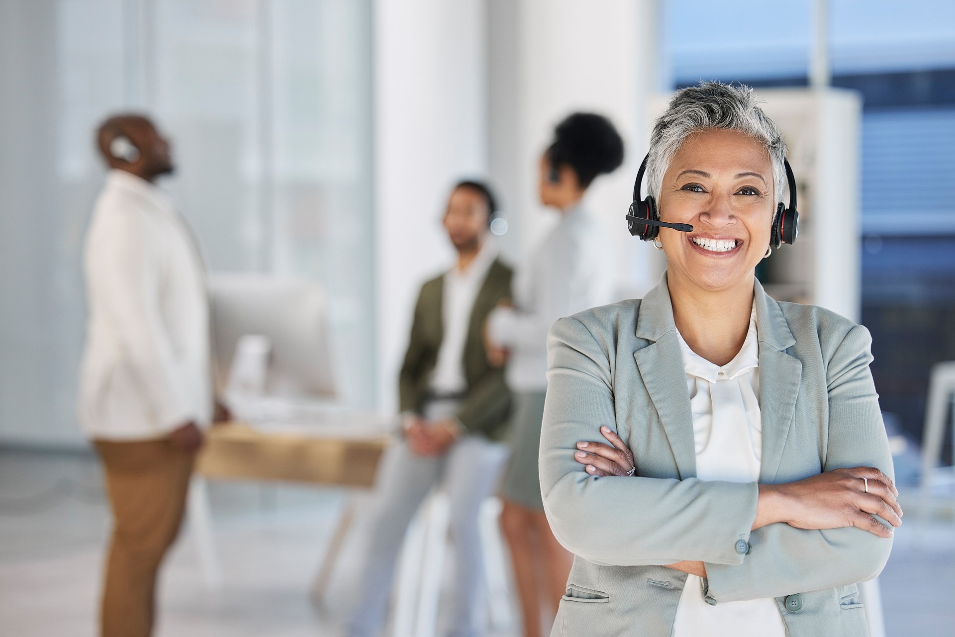 Senior woman, call center portrait and smile with arms crossed, teamwork and happiness by blurred background. Happy crm consultant, customer service expert or tech support leader in office for vision