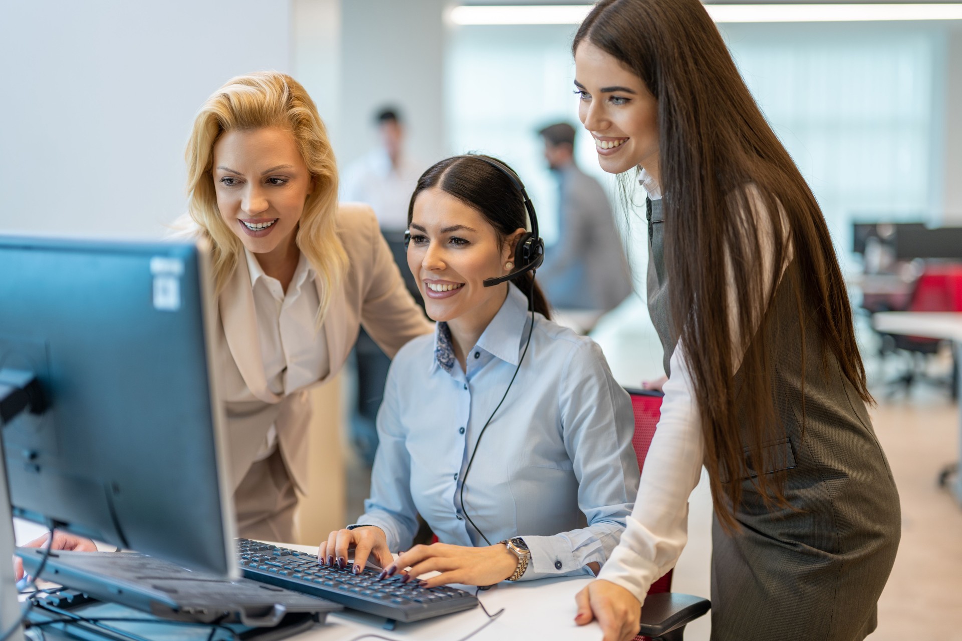 Call center woman working on computer with assistance of two female coworkers in the office.