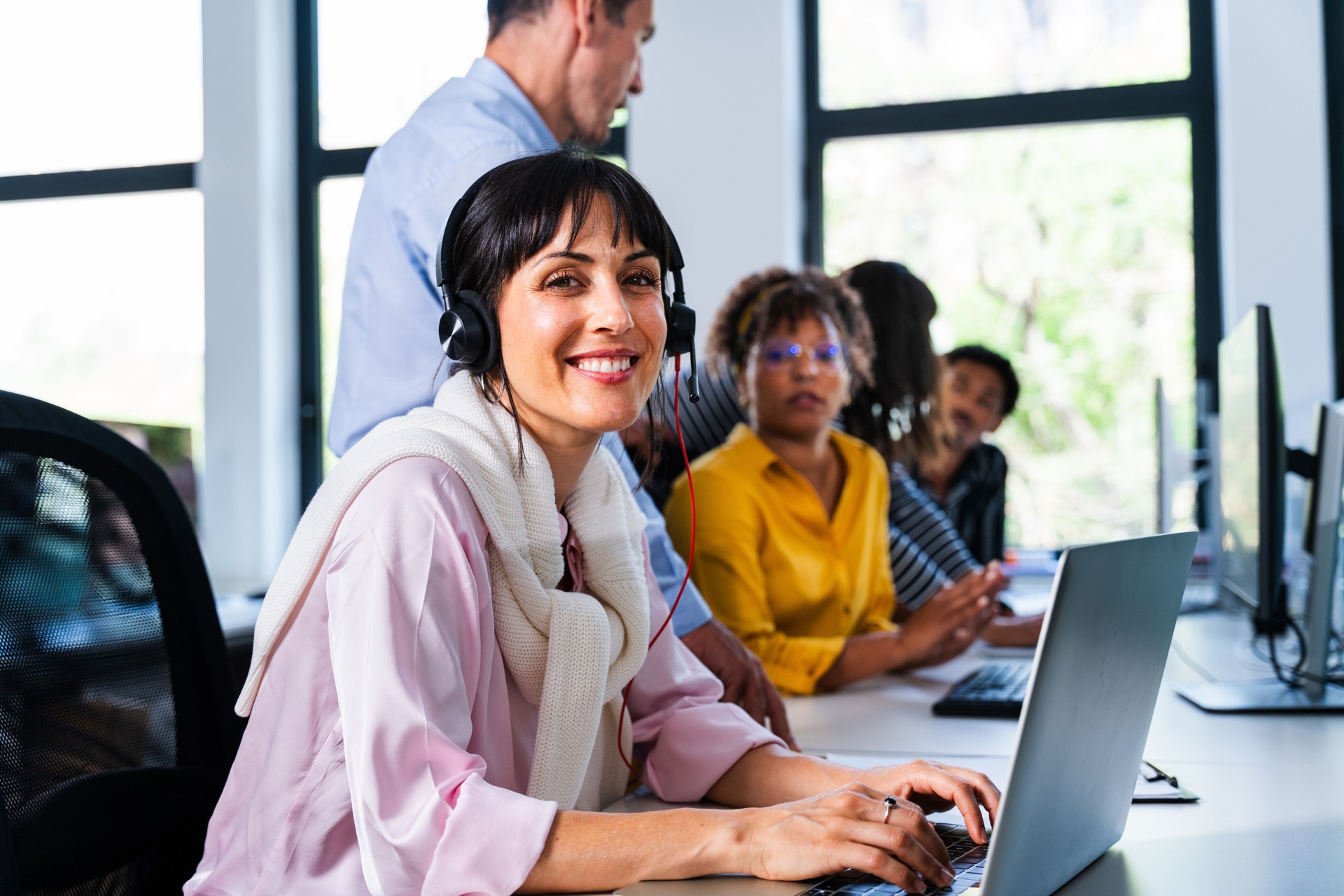Customer service representative smiling and working on laptop in busy office